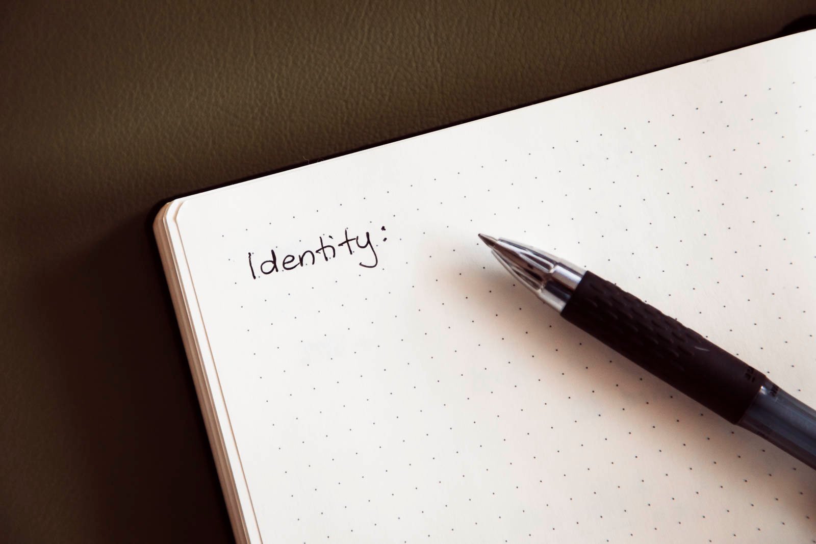 An open dot grid notebook page with word "Identity" written on it, with a pen